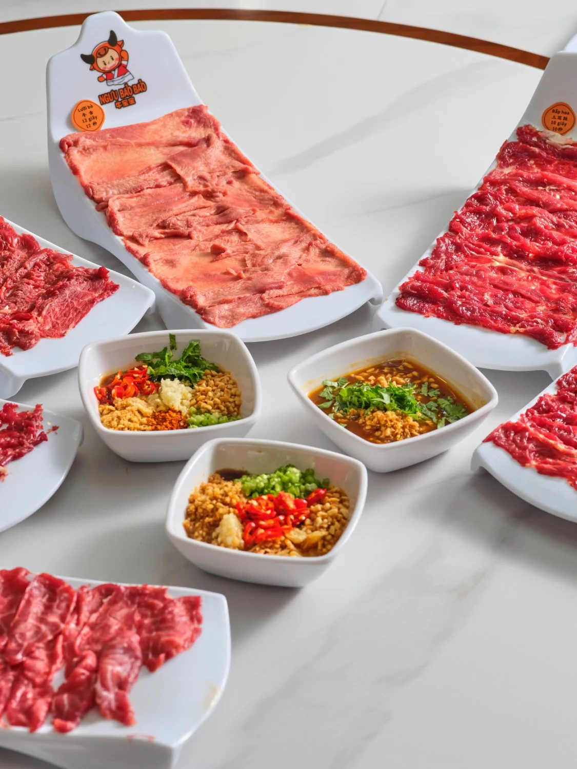 Chén Sốt chấm vị Triều Châu phối trộn rực rỡ sắc màu hành ngò, tỏi phi và sa tế độc quyền, bên cạnh là muôi múc đầy bắp hoa bò đang nghi ngút khói